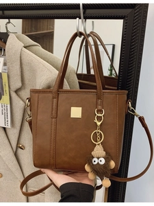 Brown faux leather tote bag with monster charm and gold buckle on a beige coat background