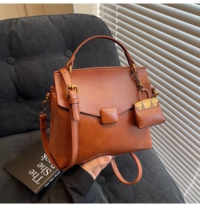Detail of a brown leather crossbody bag with top handle and matching mini charm pouch