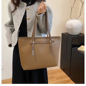 Close-up of brown pebbled leather tote bag with elegant handle and fashion text detail