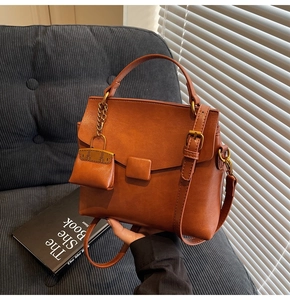 Close-up of brown litchi grain leather handbag with matching charm on a gray sofa