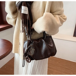 Détail du sac nuage marron foncé texturé avec pendentif rétro sur une surface en bois