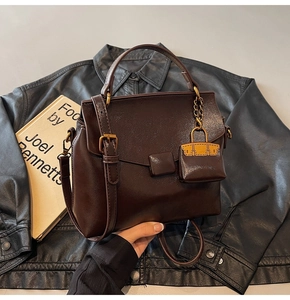 Detail of dark brown vintage underarm bag with mini charm on a leather jacket background