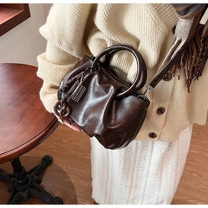 Gros plan d'un sac nuage plissé marron foncé brillant avec breloque sur pull en maille