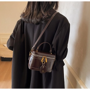 Rear view of a model wearing the dark brown glossy leather box bag with adjustable strap