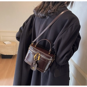Detail view of deep chocolate glossy box bag with gold double zippers and MICHTAM leather tag