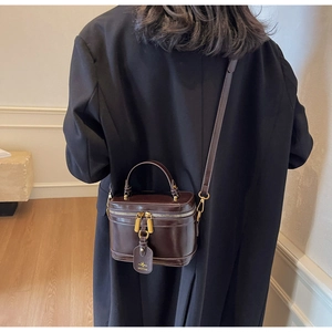 Dark brown leather box bag with gold hardware worn as a crossbody by a model in a suit