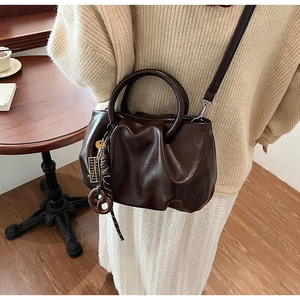 Détail d'un sac à main plissé marron foncé avec poignée ronde et breloque bretzel