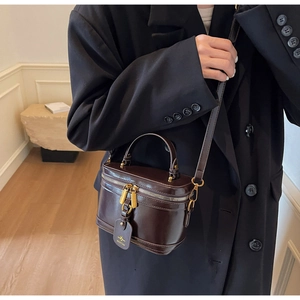 Detail of a dark brown vintage box bag with gold double zippers and a leather brand tag