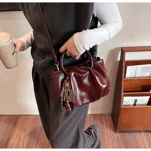 Détail du sac plissé bordeaux avec garnitures métalliques et pompon sur la bandoulière fine