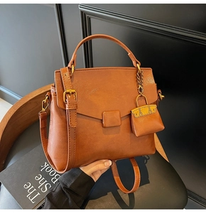 Detail of a brown leather shoulder bag with a mini charm on a black textured chair