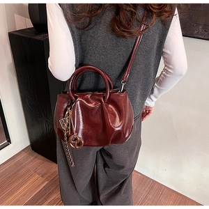 Détail du sac seau plissé en cuir bordeaux montrant la texture brillante et l'anse en métal