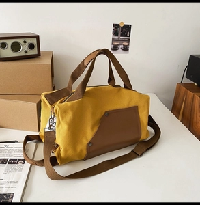 Detailed view of yellow canvas travel bag with leather handles on a retro white table