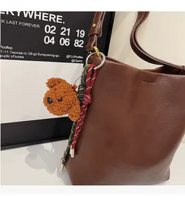 Detail of dark brown leather bucket bag with a cute teddy bear plush charm and colorful rope
