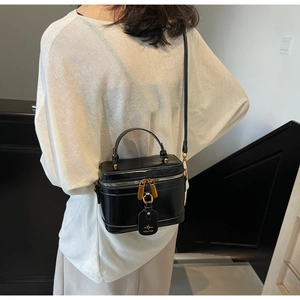 Detail of a black glossy vanity box bag with gold-tone hardware and side brand tag