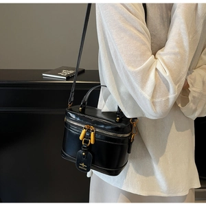 Detail of black box bag featuring polished gold hardware and logo hangtag worn on body