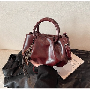 Vue détaillée du sac seau plissé bordeaux avec poignée en métal et pompon décoratif