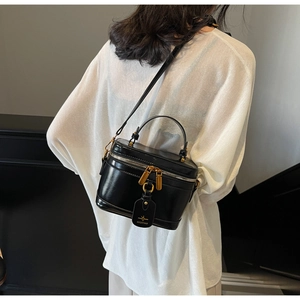 Detail of a black glossy box bag with gold hardware worn by a model in white