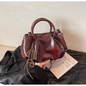 Détail du sac à main plissé en cuir bordeaux avec poignée ronde et pompon décoratif