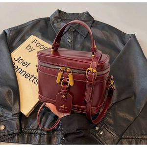 Detailed view of luxury burgundy box bag with dual zippers on a black leather jacket