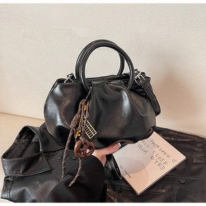 Détail du sac seau plissé noir avec poignées circulaires et pendentif décoratif