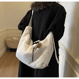 Detail view of white plush dumpling bag with wide leather strap and baseball charm detail