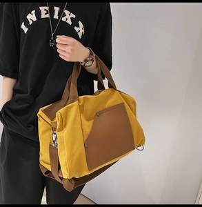 Detail view of yellow canvas boston bag with brown strap and riveted side pocket