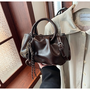 Détail d'un sac seau plissé marron foncé avec poignée en anneau métallique et pompon