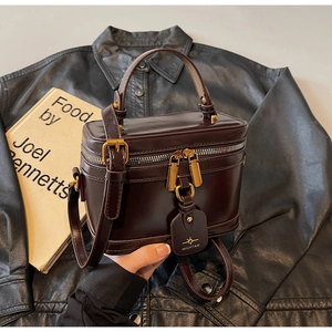 Detailed close-up of dark brown box bag with gold double zippers and premium leather tag
