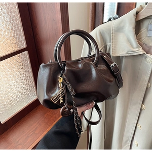 Détail du sac plissé marron foncé avec breloques vintage dorées et texture cuir brillant