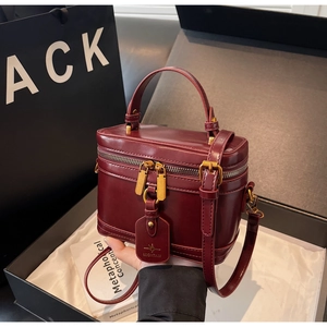 Close-up of a burgundy box bag with glossy leather and gold hardware in premium gift packaging