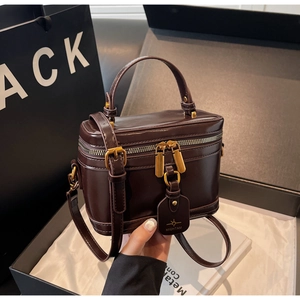 Detail of dark brown box bag featuring glossy leather texture and gold hardware accessories