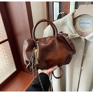 Détail d'un sac seau vintage en cuir marron avec anses en métal et pompon tissé élégant