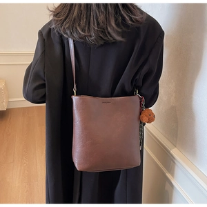 Brown bucket bag on person featuring cute dog charm and polished leather texture