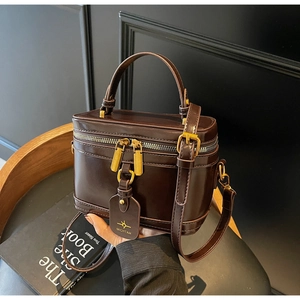 Detail of dark brown glossy box bag with gold zipper and MICHTAM logo tag in a vintage setting