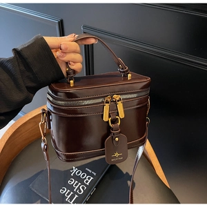 Detail of a dark brown box bag with gold double zippers and a thick top handle