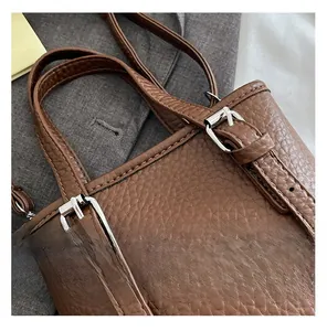 Close-up of dark brown lychee grain leather texture with silver metal buckle and stitching