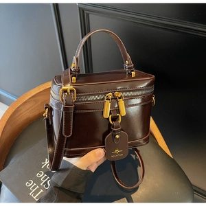 Detail of dark brown leather box bag featuring a brand tag and vintage brass hardware