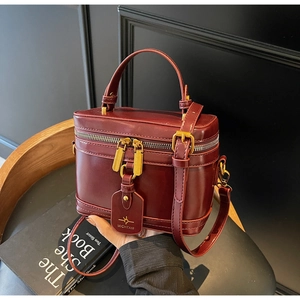 Detail of burgundy vanity bag with golden zippers, leather handle and logo tag