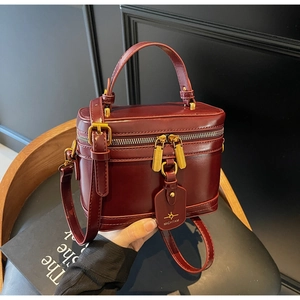 Detail view of burgundy box bag with gold metal zippers and leather hangtag on chair