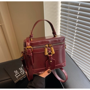 Detail of burgundy box bag in glossy leather with gold hardware and top handle