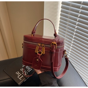 Detail of burgundy box bag featuring dual gold zippers and a branded leather tag