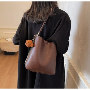 Detail view of dark coffee bucket bag with a cute brown plush teddy bear charm accessory