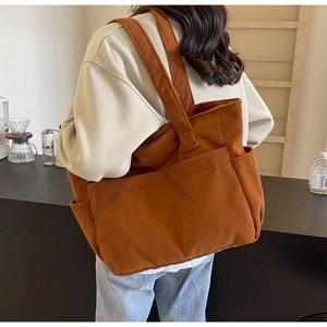 Vue arrière du modèle portant un grand sac cabas en velours côtelé caramel dans un café