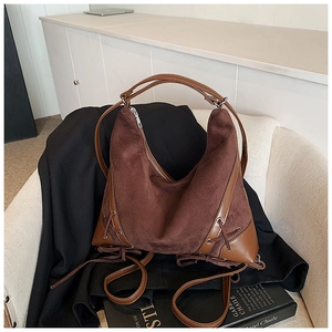 Detail of a brown suede and leather shoulder bag resting on a sofa with an art book