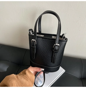 Detail of black pebbled leather bucket bag with silver buckles and handle held by model