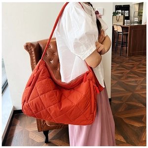 Detailed side view of orange quilted nylon tote bag with classic diamond stitching