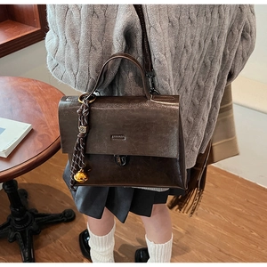 Detail einer dunkelbraunen Lackledertasche mit Schnalle und gewebtem Glockenanhänger