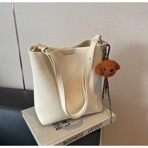 Detail of minimalist cream bucket bag with a cute brown teddy bear plush charm