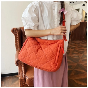 Detail view of large orange quilted nylon tote bag worn with adjustable strap over the shoulder
