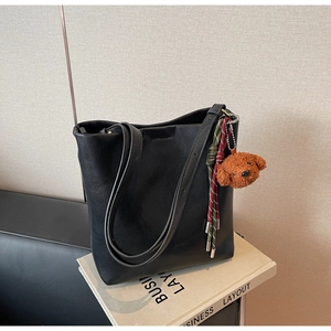 Close-up of black textured leather tote bag with cute plush puppy and rope charms